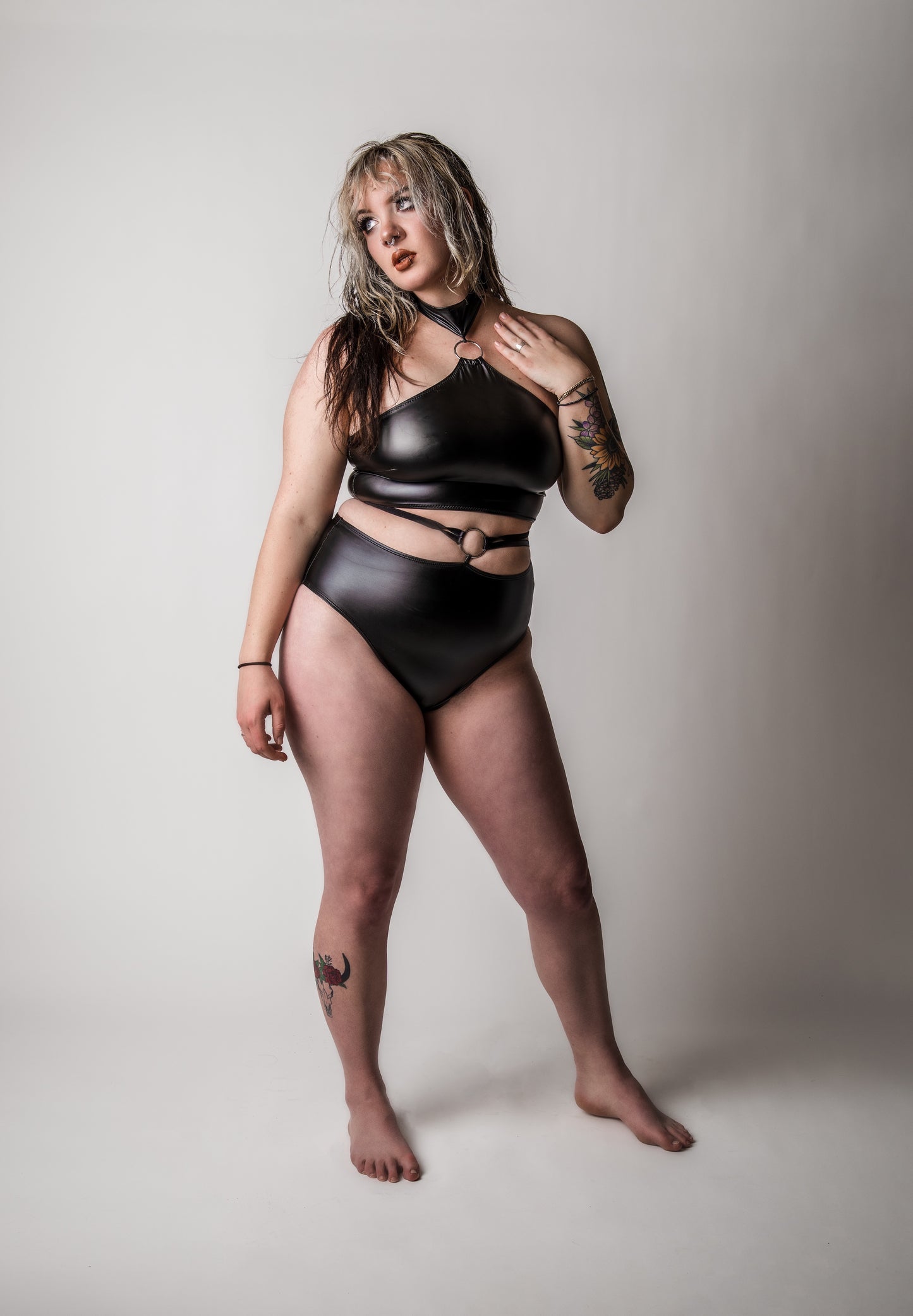 Image of high quality faux leather two piece set consisting of a halter top with metal O ring and high rise bottoms with metal O ring and elastic sides, on female model with a white background.